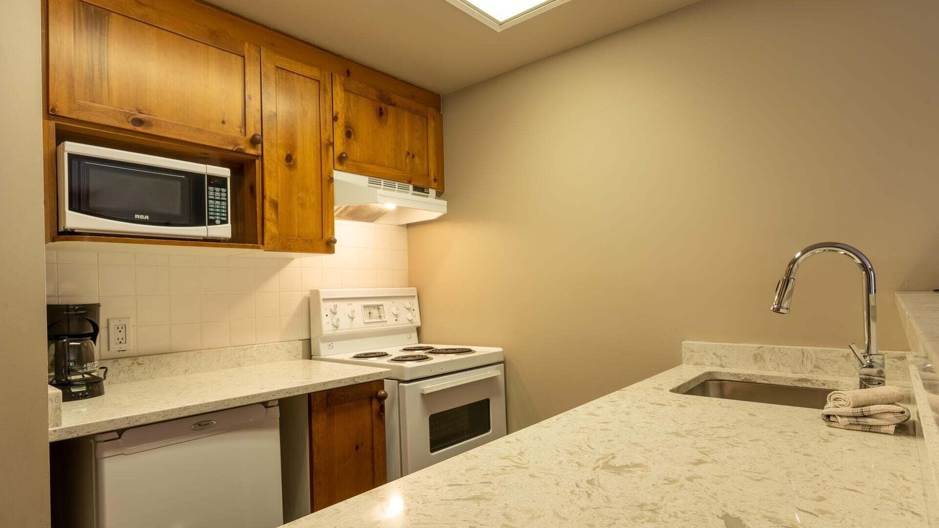 A kitchen with wooden cabinets, a microwave, a stove, a dishwasher, and a sink with a towel.