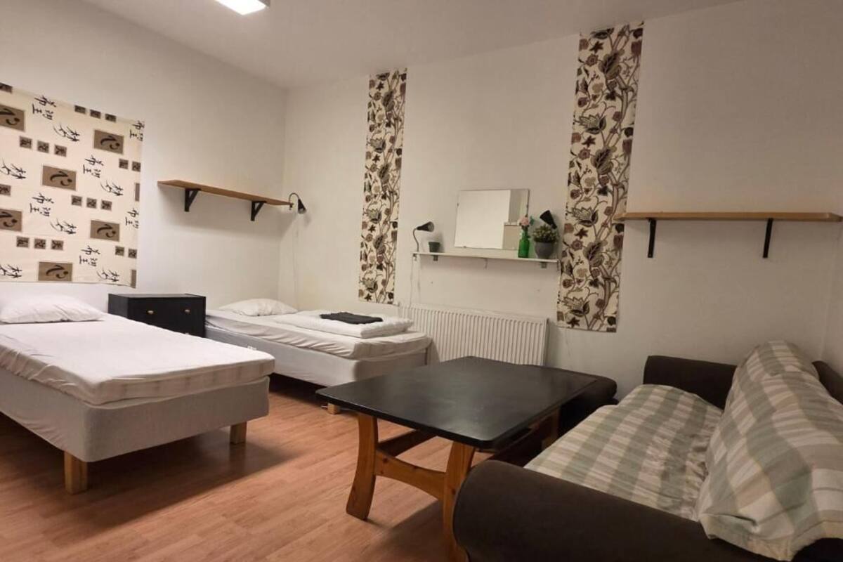 A room with two beds, a small table, a sofa, and a radiator.