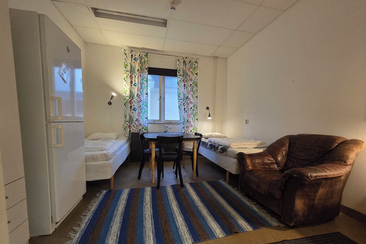 A small, compact room with a bed, a desk, a chair, and a refrigerator.