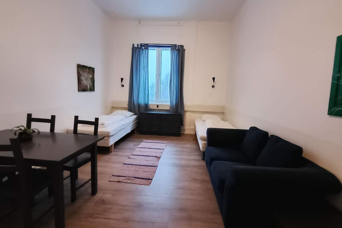 A compact room with a bed, a sofa, a table, and a window with curtains.