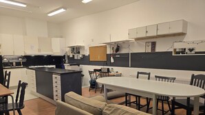 A compact kitchen with a dining area, featuring a central island, white cabinets, and a black countertop. - Svenshögens vandrarhem (Svenshögen)