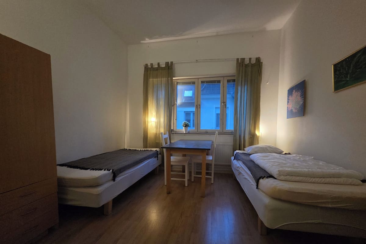 A small, cozy room with two single beds, a wooden desk, and a chair.