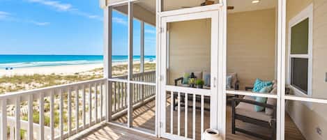 A wooden deck with a view of the beach, a seating area with cushions, and a white vase.