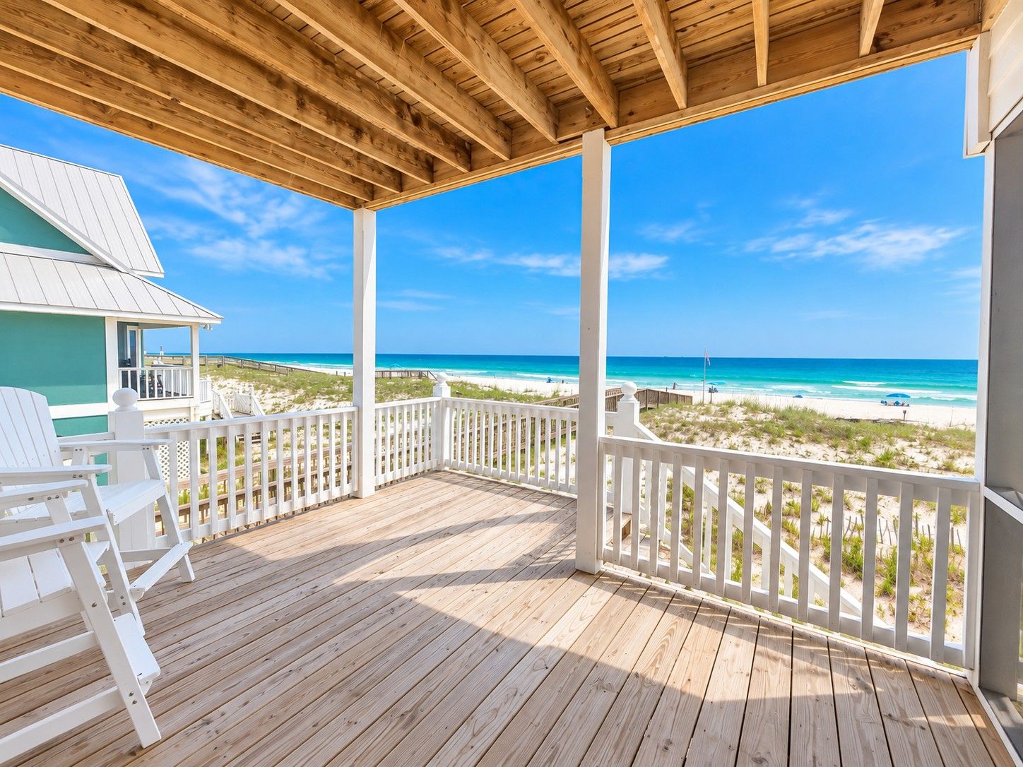 A wooden deck with white railings overlooking a beach.