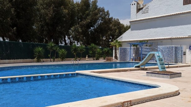 A swimming pool with a slide, surrounded by a tiled deck and palm trees. - Charming 3-bedroom House With Shared Pool in Punta Prima, Torrevieja (Torrevieja)