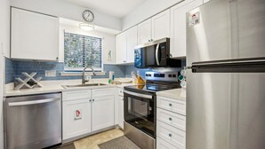 A modern kitchen with stainless steel appliances, white cabinetry, and a blue backsplash. - 4f Amelia Landings 2 Bedroom Condo (Fernandina Beach)