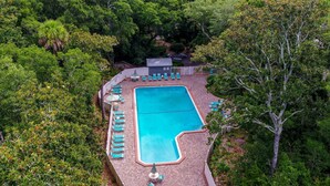 An aerial view of a rectangular swimming pool with a tiled deck, surrounded by lush greenery and trees. - 4f Amelia Landings 2 Bedroom Condo (Fernandina Beach)