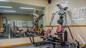 Ein Fitnessraum mit verschiedenen Trainingsgeräten, einem großen Spiegel und informativen Plakaten an der Wand.