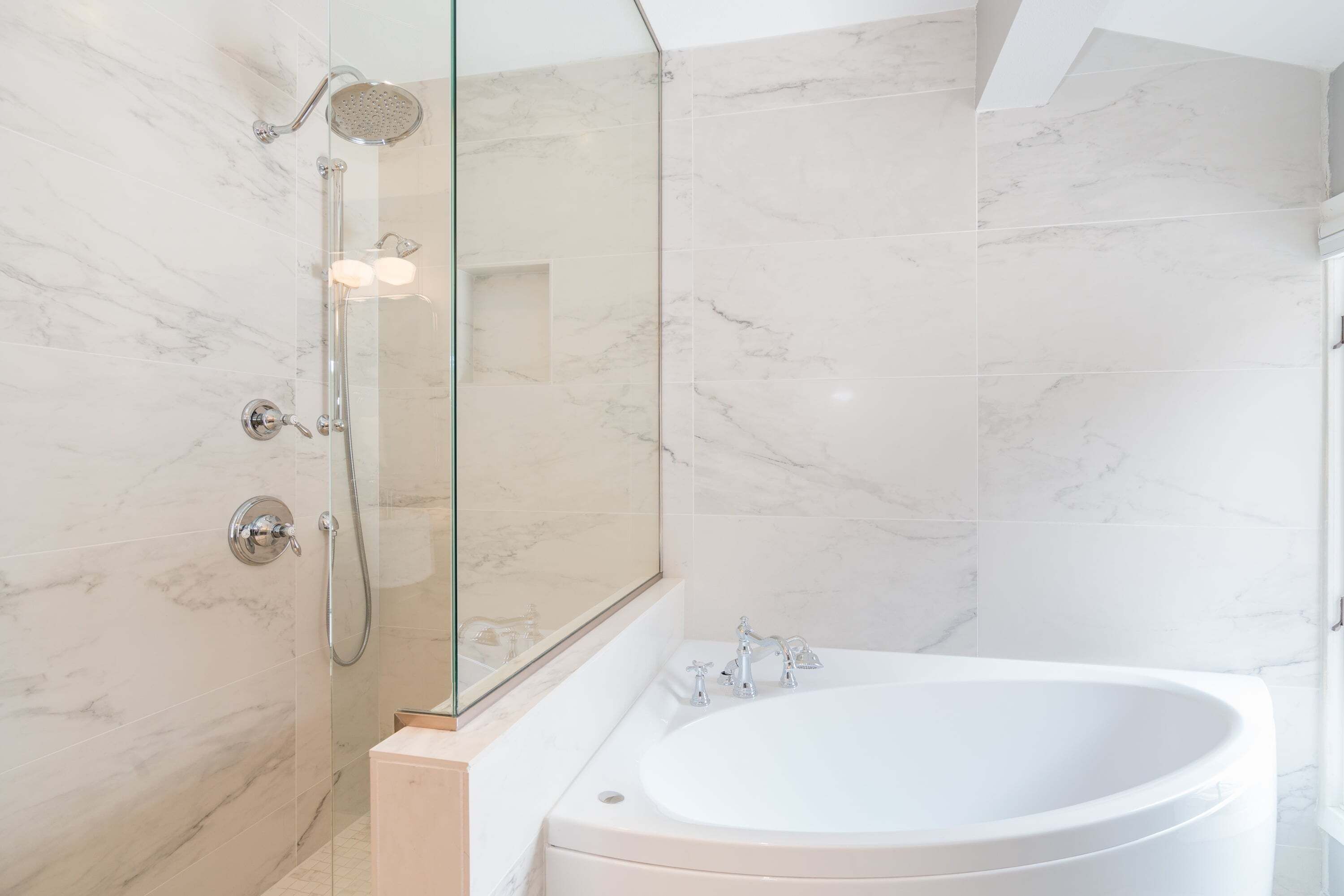 Une salle de bain moderne avec une douche à parois de verre, une baignoire sur pieds et des murs en marbre.