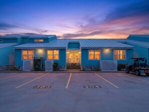 Edificio a due piani con facciata blu, parcheggio con posti delimitati e un golf cart parcheggiato davanti.