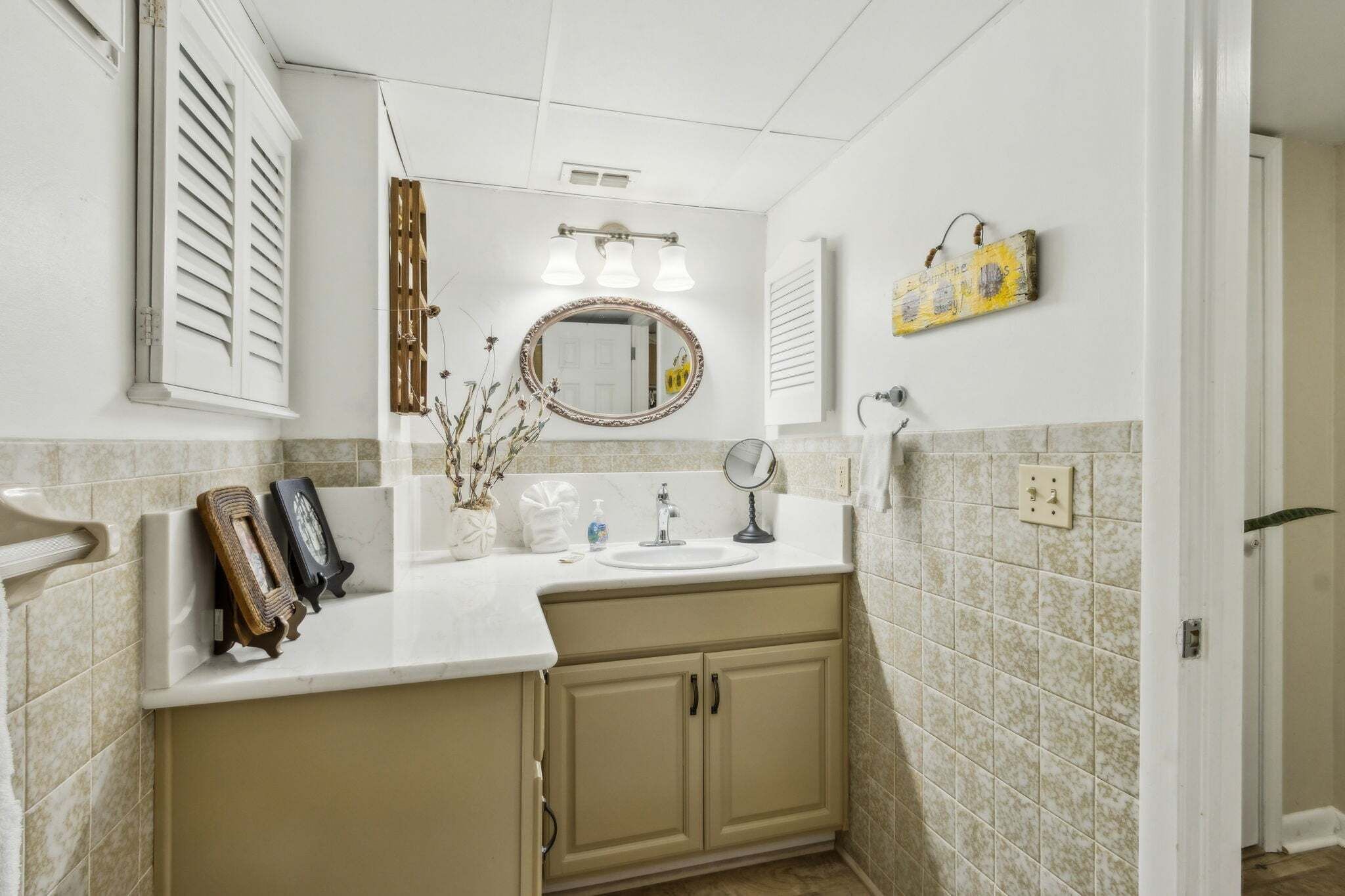 A bathroom with a sink, mirror, and towel rack. There are two towel racks, a mirror, and a light fixture above the mirror.