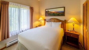 A hotel room with a large bed, two bedside tables with lamps, a painting on the wall, and a window with curtains.