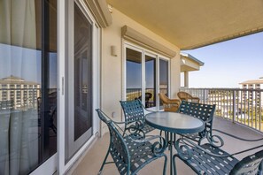Un balcone con un tavolo rotondo e quattro sedie, ampie porte scorrevoli in vetro e vista sui palazzi sullo sfondo.
