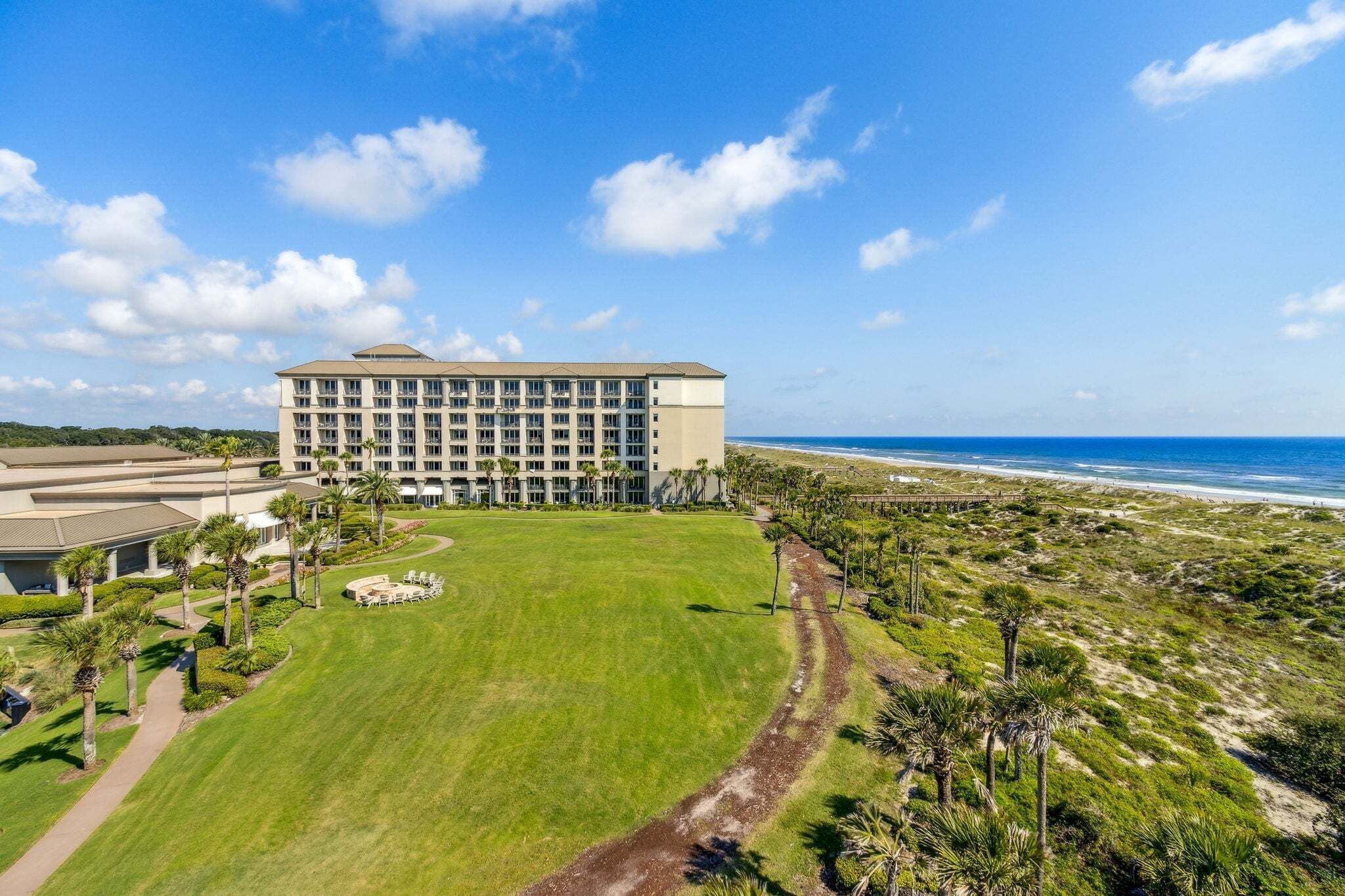 Ein Hotel mit einem großen Gebäude, einer Grünfläche und einem Strand im Hintergrund.