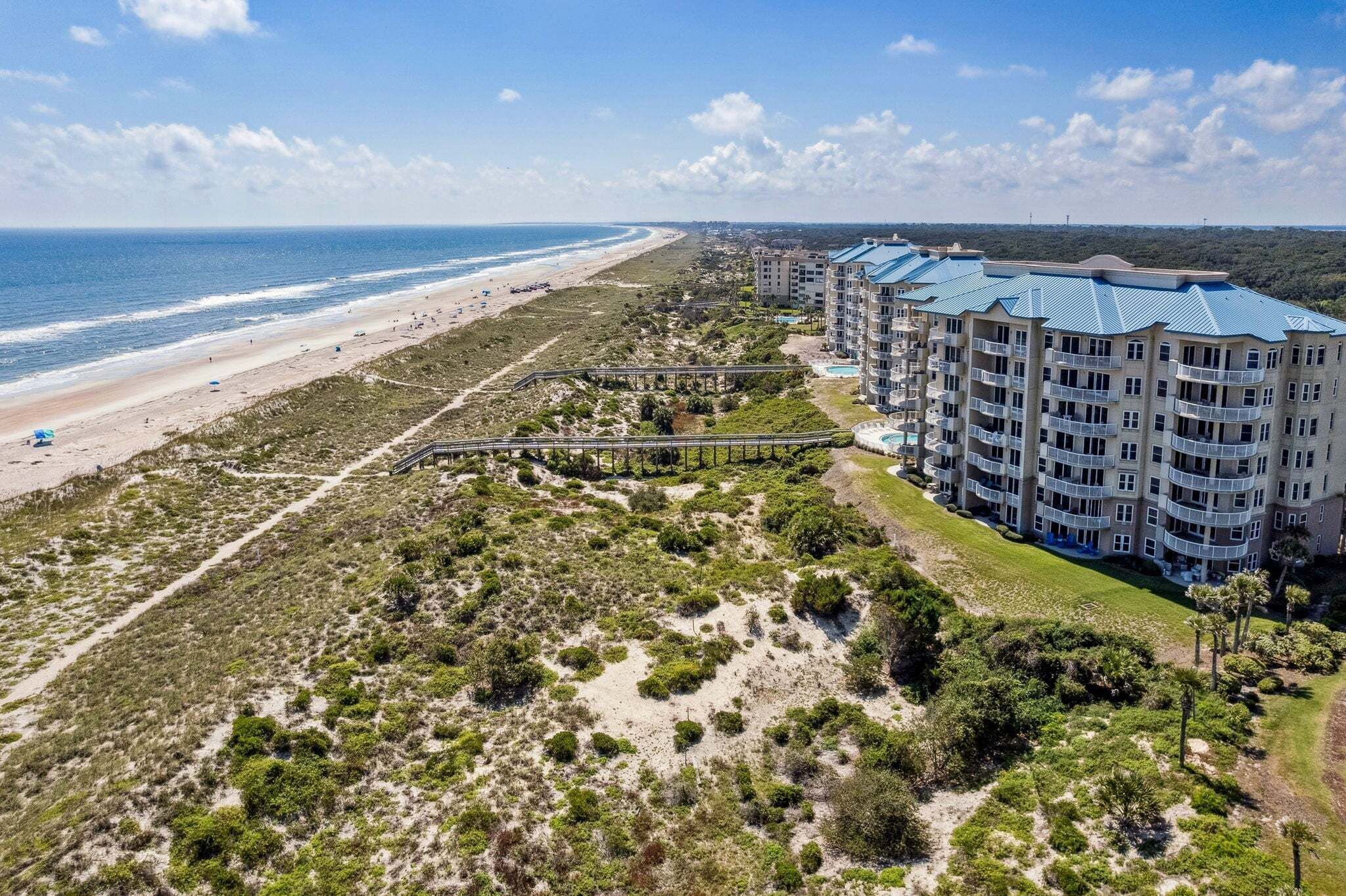 A beachfront hotel with multiple balconies, a swimming pool, and a beach access path.