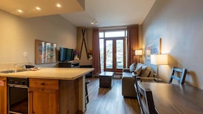 A modern kitchen with a central island, a dining area with a table and chairs, and a living room with a sofa and a TV.
