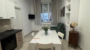 Un espace de vie compact comprenant un coin cuisine, un coin repas et un espace détente avec un canapé et un téléviseur fixé au mur.