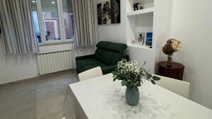 Un salon moderne avec un canapé vert, une table à manger agrémentée d’un vase de fleurs et un radiateur blanc.