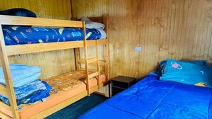 Une chambre avec un lit superposé, avec un lit en bas et un lit simple en haut. La chambre contient une petite table et une chaise.
