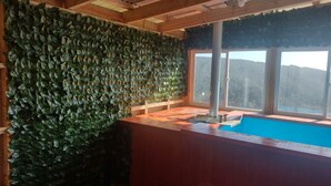 Une pièce avec un plafond en bois, une grande fenêtre donnant sur les montagnes et un mur recouvert de feuillage verdoyant.
