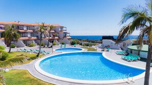 Een resort met een groot zwembad, ligbedden en uitzicht op de oceaan.