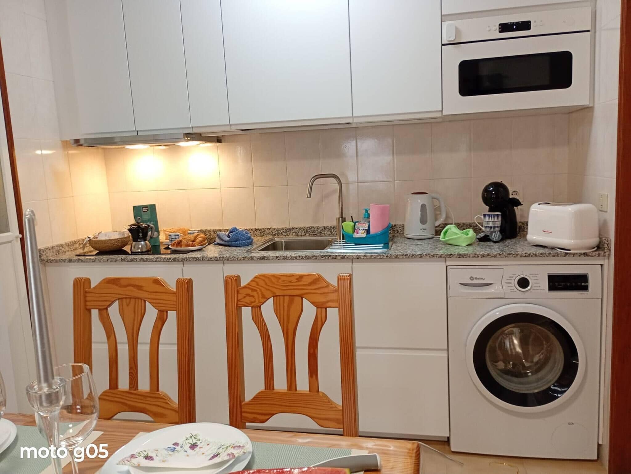 Una cocina compacta equipada con lavadora, microondas y fregadero.