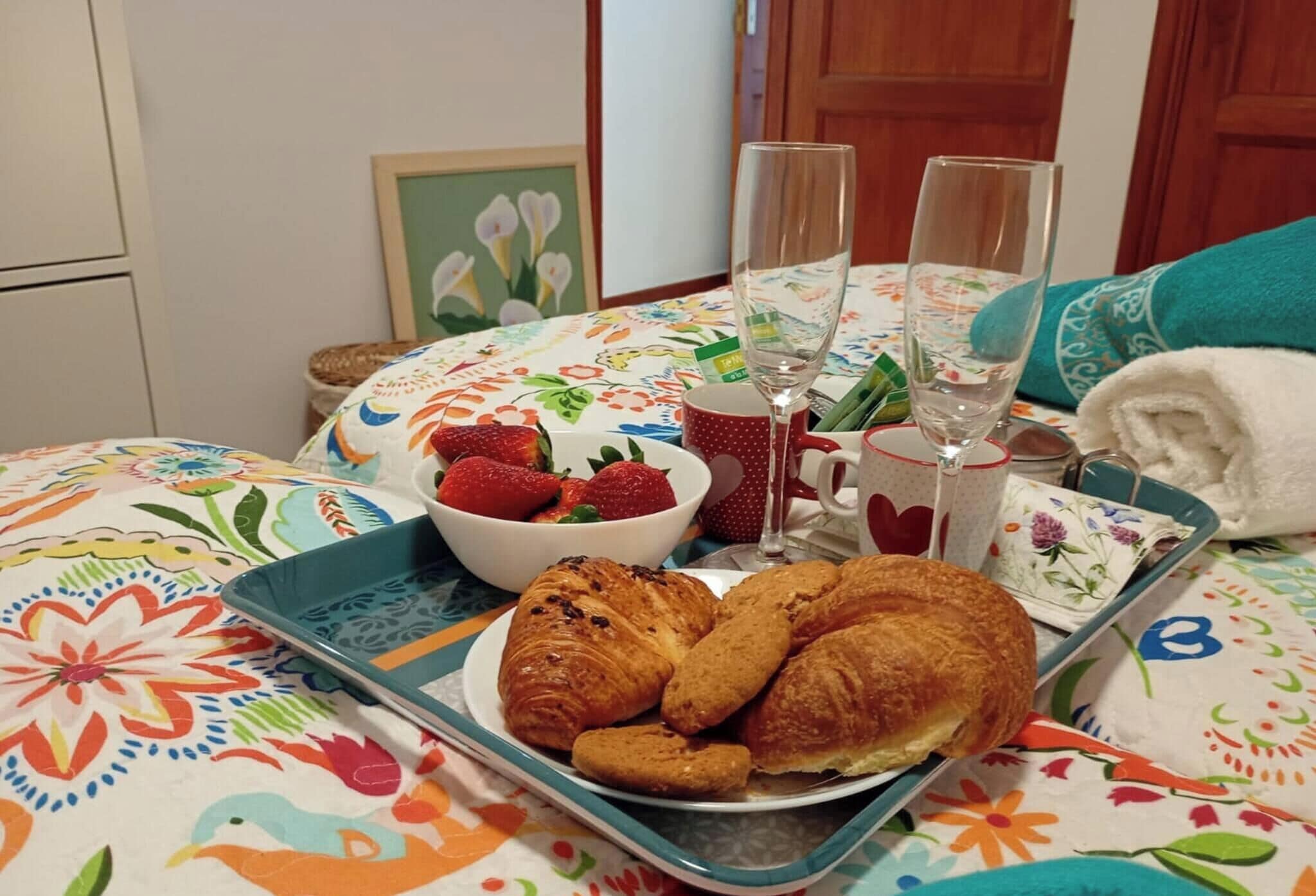 Un safata d'esmorzar amb croissants, freses i un bol de fruita sobre un llit amb un estovat floral.
