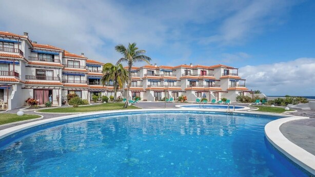 Een resort met een groot zwembad, meerduizelinge gebouwen en uitzicht op de oceaan.