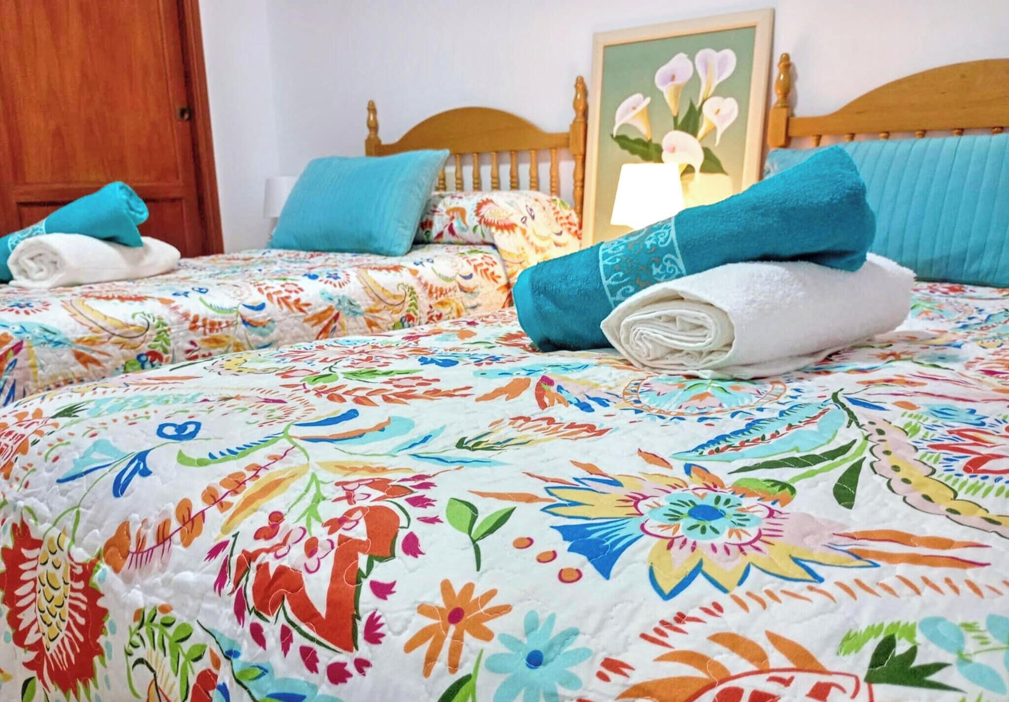 Habitación de hotel con dos camas, ropa de cama estampada con motivos florales y un cabecero de madera.