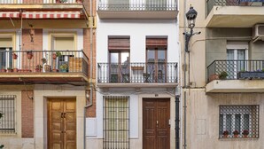 A row of three-story buildings with balconies, wooden doors, and potted plants. - El Mirador de Neptuno: Your Private Balcony Over Priego de Córdoba’s History (Priego de Córdoba)