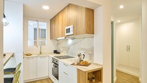 A modern kitchen with white cabinetry, a wooden upper cabinet, a microwave, a stove, and a small wooden shelf with a pineapple. - El Mirador de Neptuno: Your Private Balcony Over Priego de Córdoba’s History (Priego de Córdoba)
