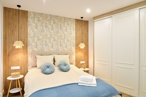 Ein Schlafzimmer mit Bett, zwei Nachttischen, einem Schrank und einer Wand mit vertikalen Holzpaneelen und floralem Wandpapier.