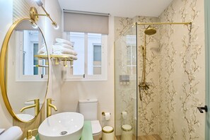 Ein Badezimmer mit großem Spiegel, Waschbecken, Toilette, Duschkabine mit Glastüren und einem Fenster.