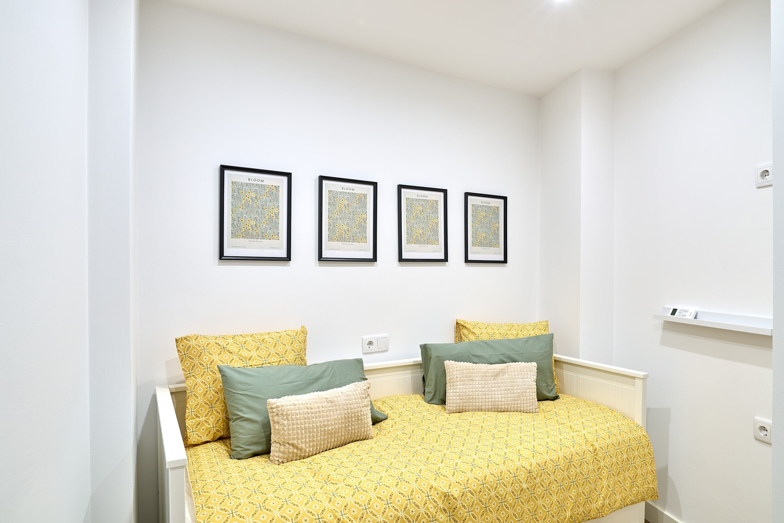 Une chambre à coucher avec un lit double, deux tables de chevet, un mur blanc et quatre tableaux encadrés.