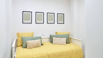 A bed with a yellow patterned bedspread, two pillows, and a white headboard. There are three framed pictures on the wall above the bed.