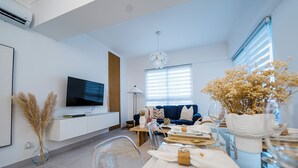 Ett modernt vardagsrum med en platt-TV, en soffa och en matplats med ett bord dukat för två personer.