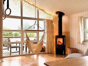 Ein Zimmer mit Hängematte, Kamin und großen Fenstern.