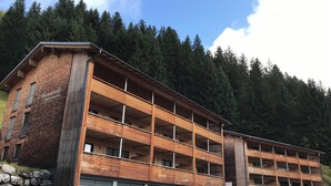 A multi-story building with a wooden facade and a stone wall on the left. - House Annabelle Top 1 (Damüls)
