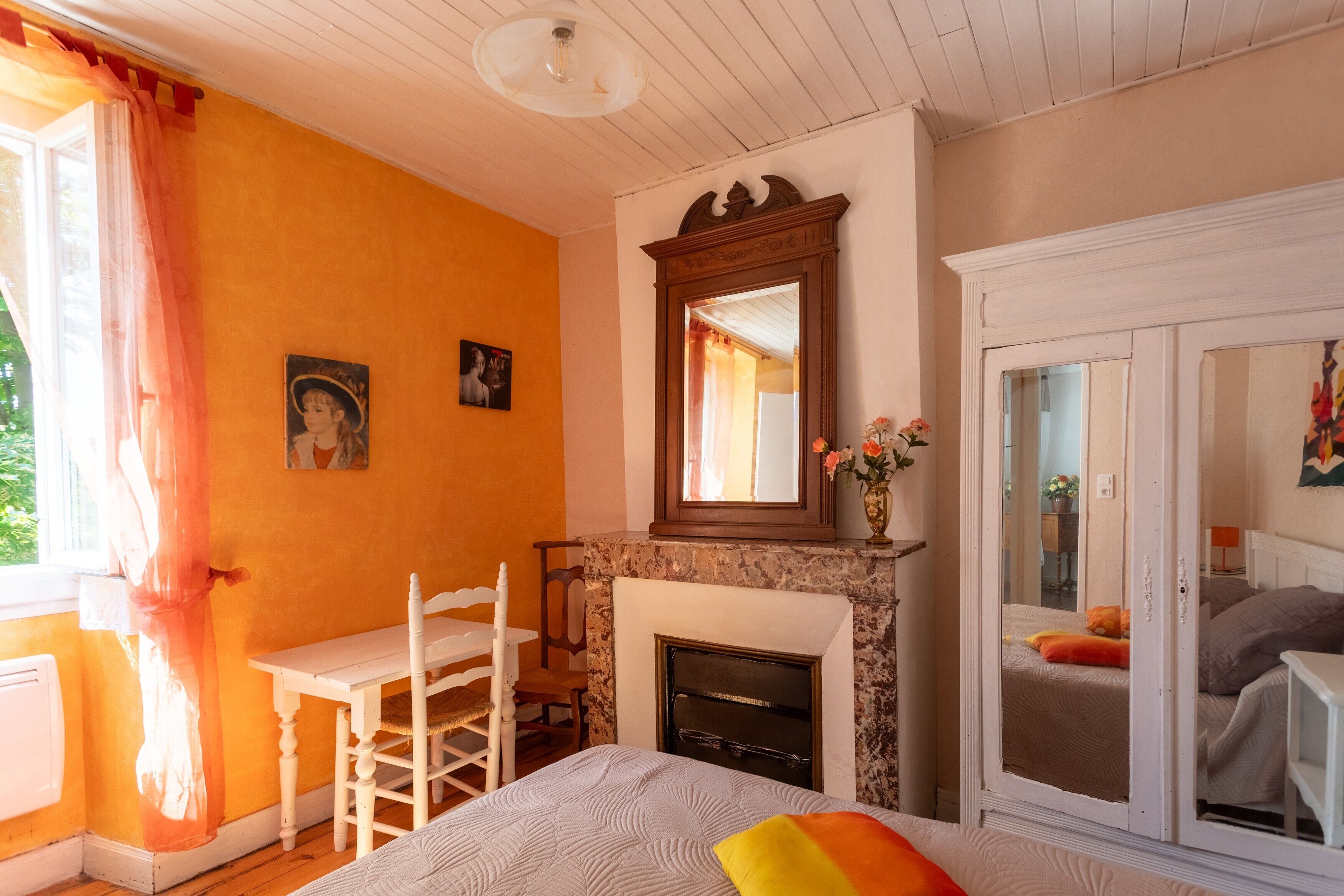 Une chambre avec une cheminée, un lit avec des oreillers, un bureau avec une chaise et une fenêtre avec des rideaux.
