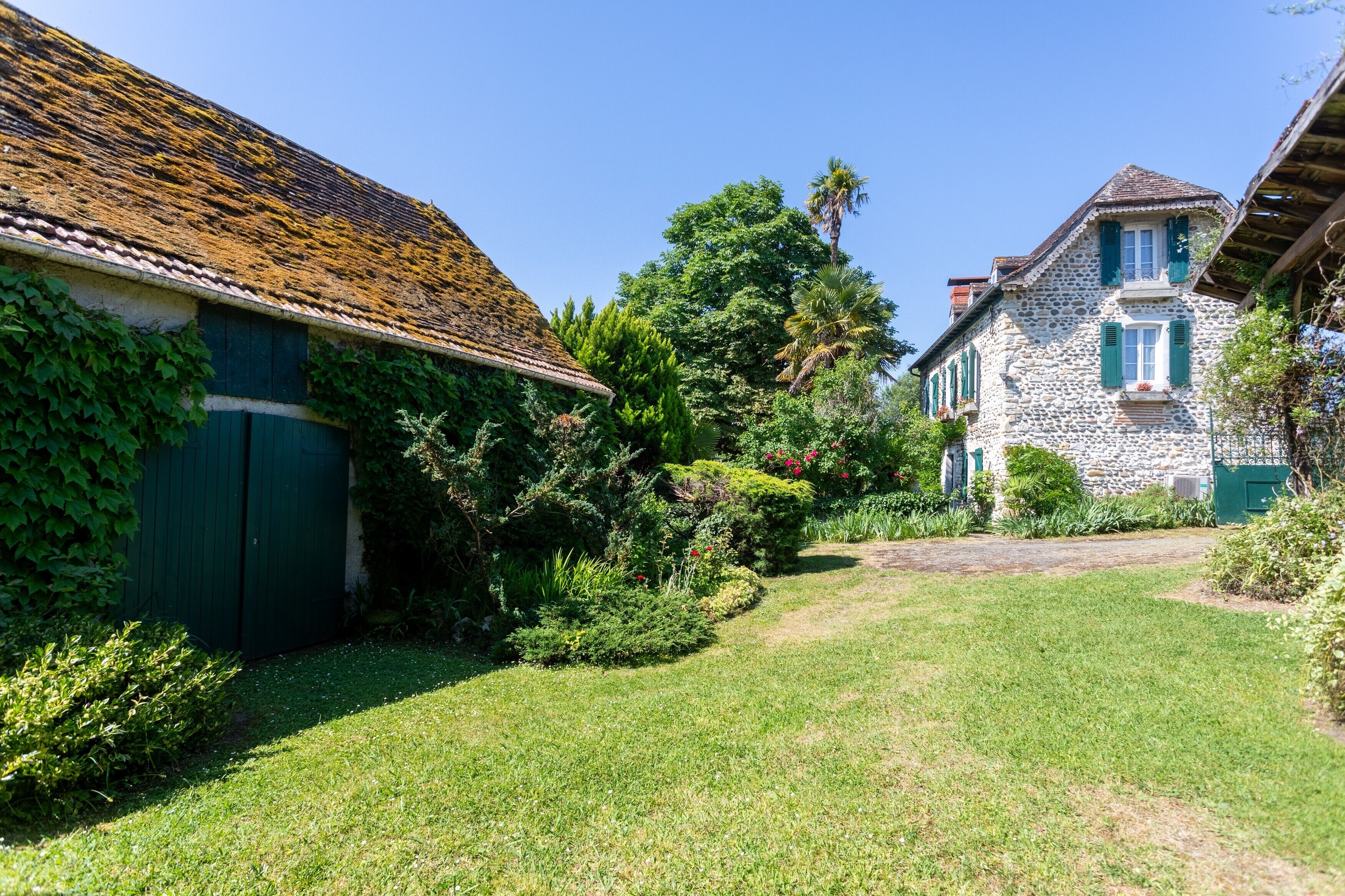 A stone building with a thatched roof, a green door, and a garden with a lawn and trees.