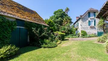 A stone building with a thatched roof, a green door, and a garden with a lawn and trees.