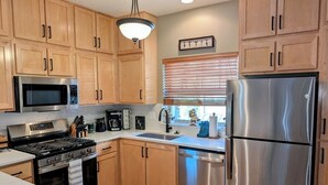 Una cocina moderna con armarios de madera, electrodomésticos de acero inoxidable y un ventanal con persianas.
