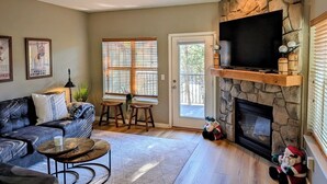 Una sala de estar con chimenea de piedra, un sofá de cuero negro, una mesa de centro y un televisor montado en la pared.