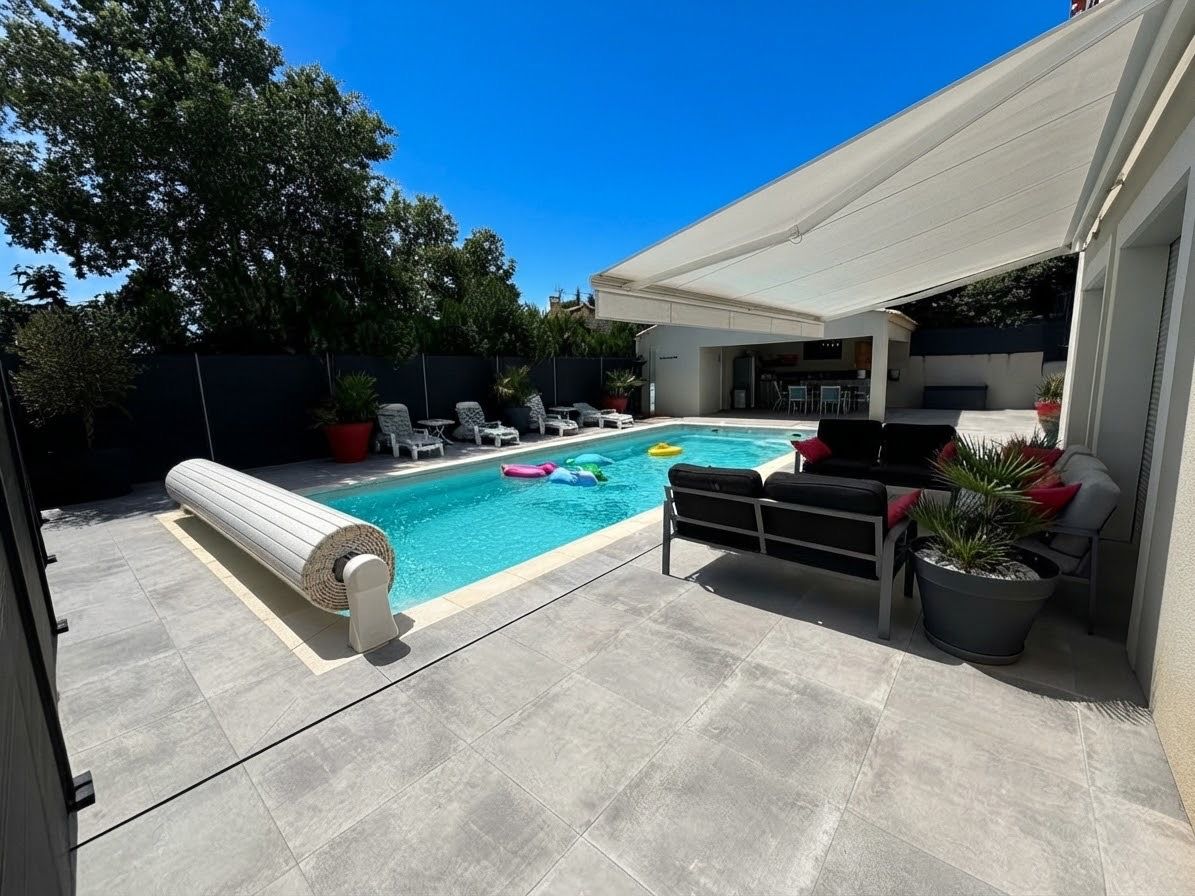 A backyard with a swimming pool, lounge chairs, and a covered patio area.