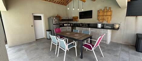 A kitchen with a wooden ceiling, a dining table with chairs, and a refrigerator.
