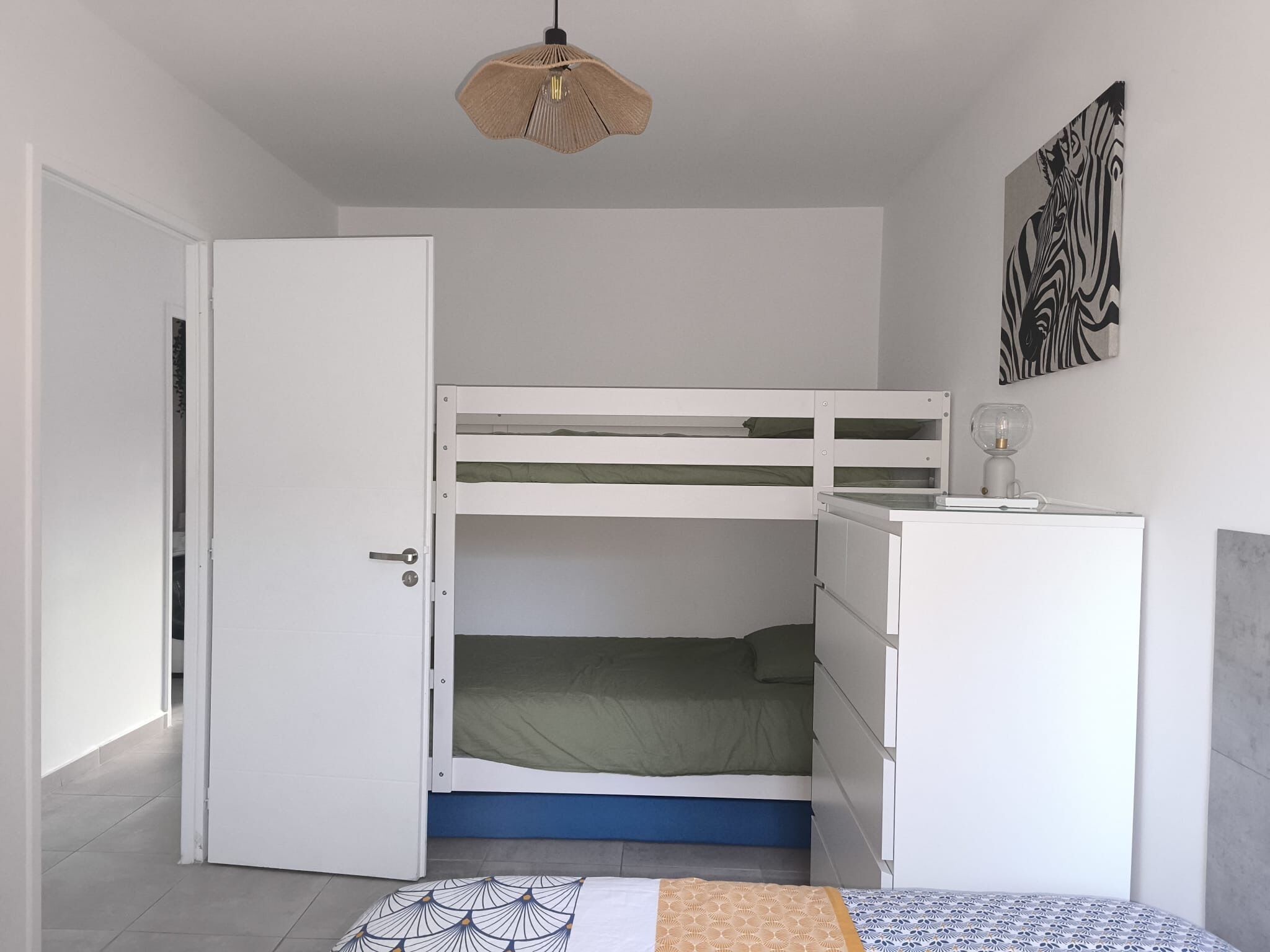 A room with a bunk bed, a desk with a lamp, a door, and a zebra-patterned artwork on the wall.