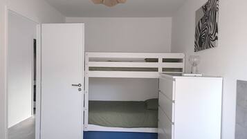 A room with a bunk bed, a desk with a lamp, a door, and a zebra-patterned artwork on the wall.