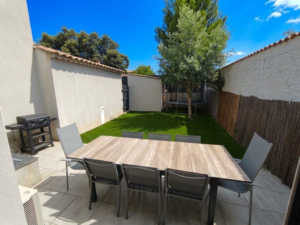 Eine Terrasse mit Holztisch und -stühlen, einem Grill und einem kleinen Baum.