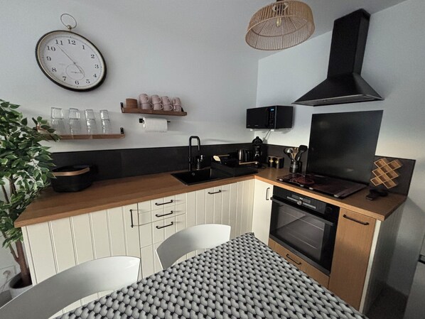 Una cocina compacta con encimera de madera, horno empotrado, un lavamanos y una zona de comedor con mantel estampado.