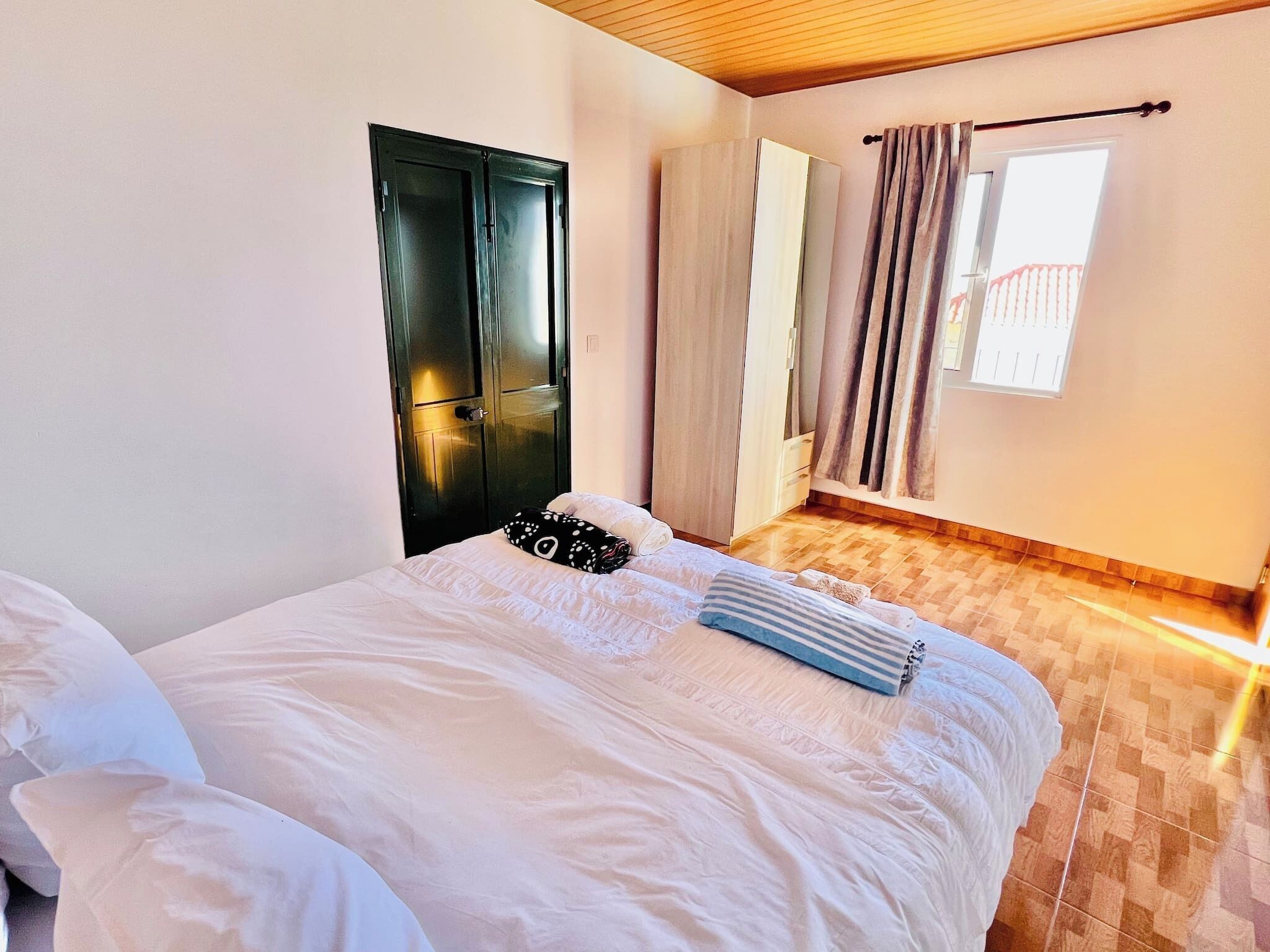 A bedroom with a bed, a wardrobe, a window with curtains, and a wooden floor.